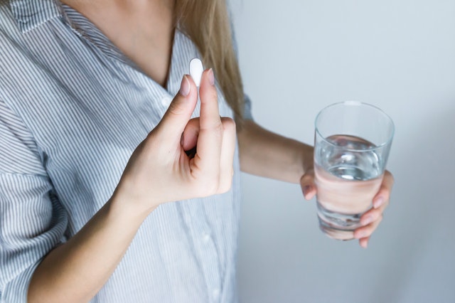 Žena drží v ruke tabletku a pohár s vodou